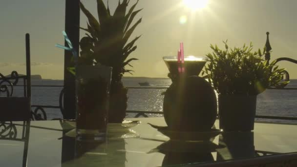 Várias bebidas em uma mesa com pôr do sol no mar atrás — Vídeo de Stock