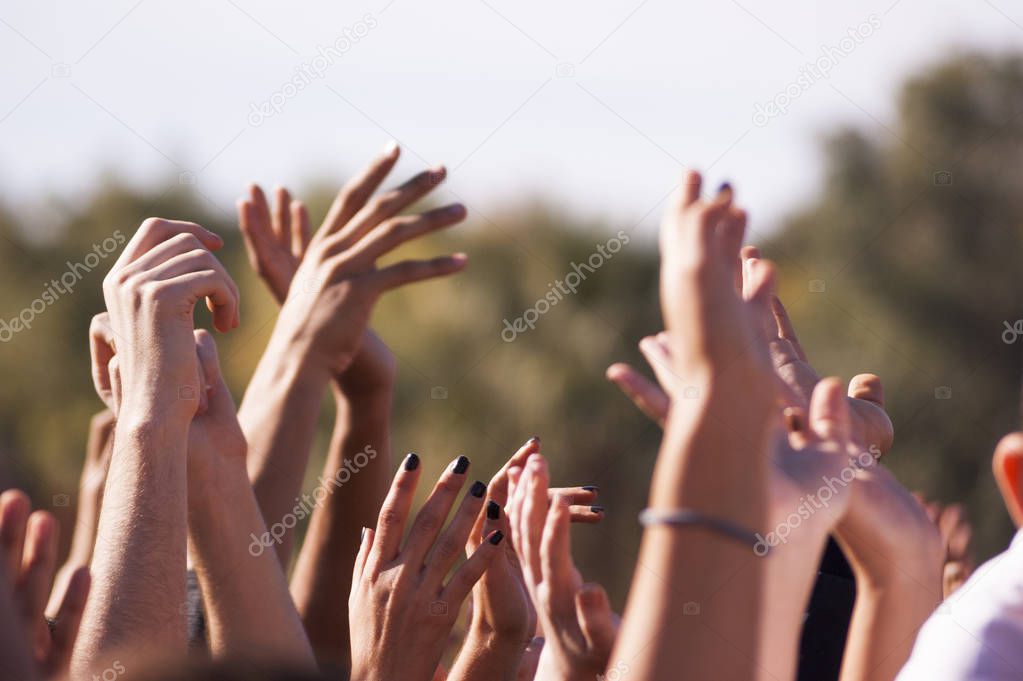 Crowded people hands up at a day time concert.