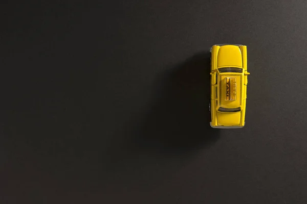 Top view of a Yellow toy Taxi car on a black background with long and side shadow.