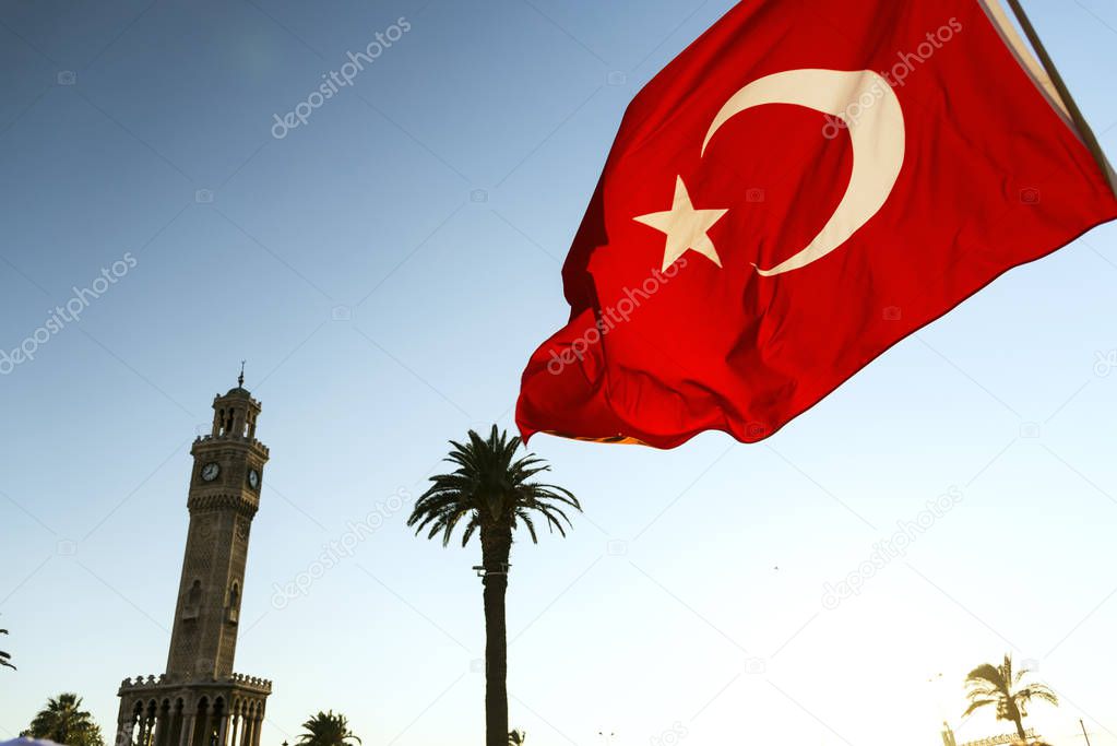 Izmirs clock tower and Turkish flag waving with palm trees.