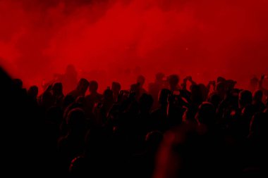 Konser alanı, kırmızı sahne ışıkları altında kalabalık kişi.