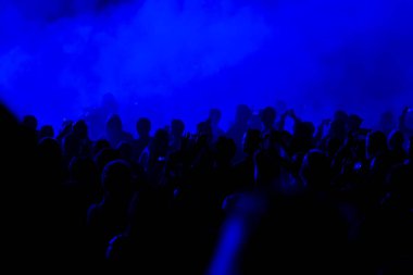 Konser alanı, mavi sahne ışıkları altında kalabalık kişi.