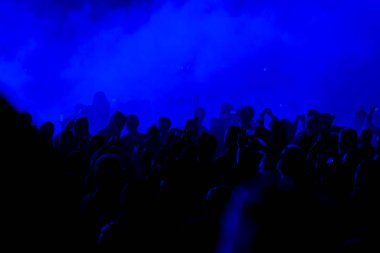 Konser alanı, mavi sahne ışıkları altında kalabalık kişi.