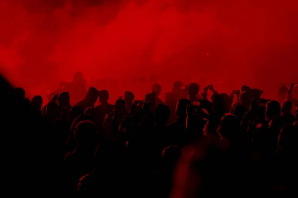 Concert field, crowded people under the red stage lights.