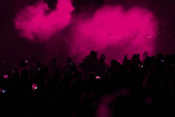 Concert field, crowded people and pink stage lights with smoke.