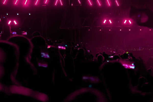 Concert field, crowded people and red stage lights with smoke.