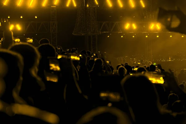 Concert field, crowded people and yellow stage lights with smoke.