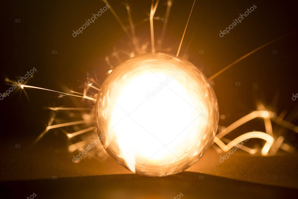 Burning sparkler behind a glass ball on a black background.