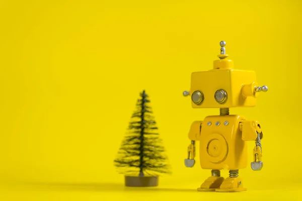 Cute, yellow, handmade robot on a yellow background with a pine tree.