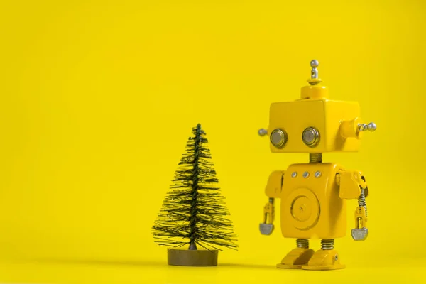 Cute, yellow, handmade robot on a yellow background with a pine tree.