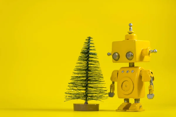 Cute, yellow, handmade robot on a yellow background with a pine tree.