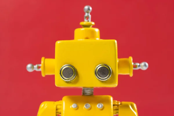 Portrait of a Cute, yellow, handmade robot on a red background.