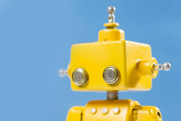 Portrait of a Cute, yellow, handmade robot on a blue background.