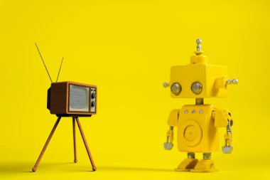 Sevimli sarı el yapımı robot bir retro televizyon ile sarı bir arka plan üzerinde.
