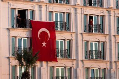 İki kişi ile bir binada asılı Türk bayrağı.