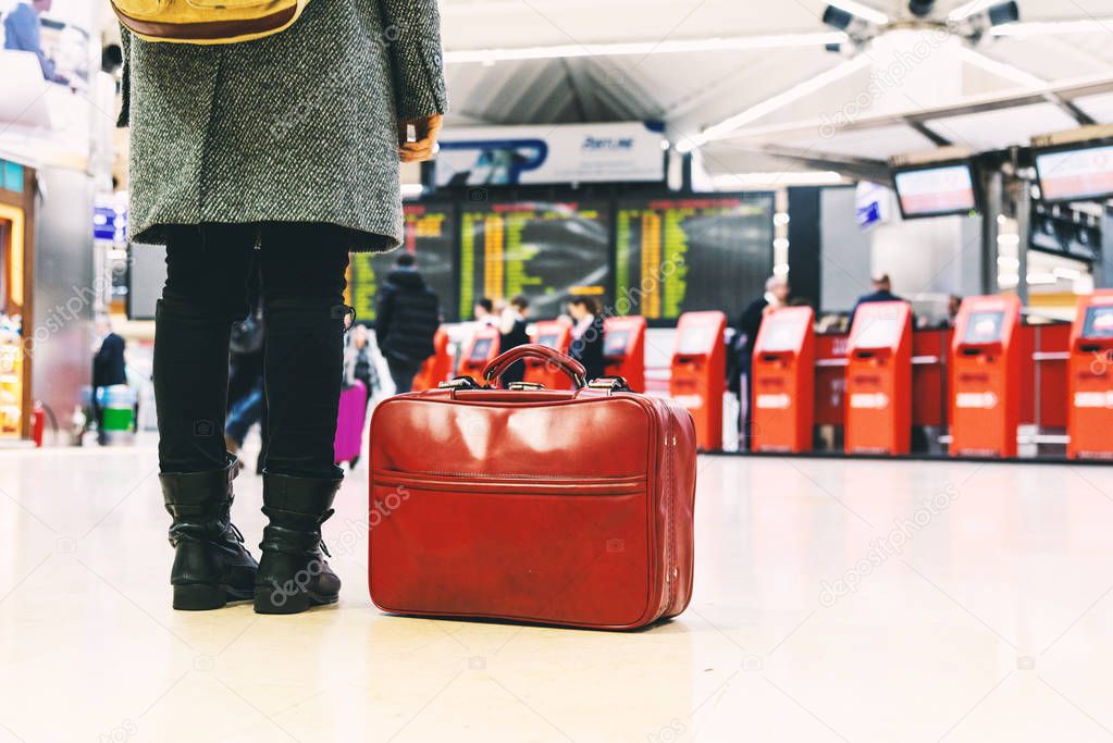 Woman with boots, coat and a red bag in an airport.