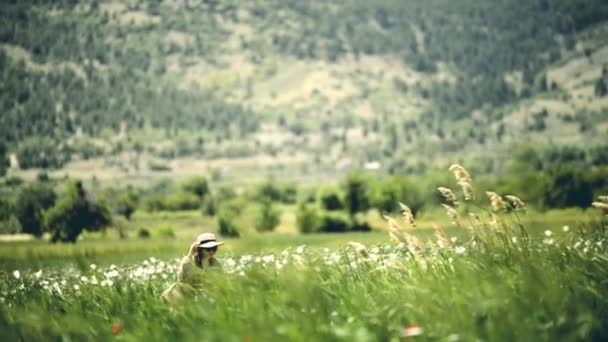 3030戴帽子和太阳镜的妇女在罂粟和一个村庄的农田之间行走 — 图库视频影像