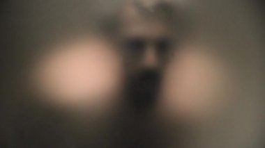 Tanınmaz korkunç ve çıplak adam dikkatle buzlu bir cam arkasına bakıyor.
