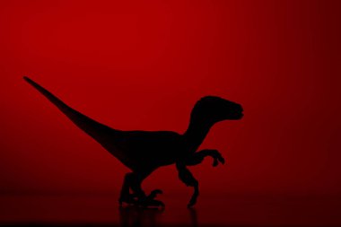 Kırmızı renkli arka planda bir dinozor silueti.