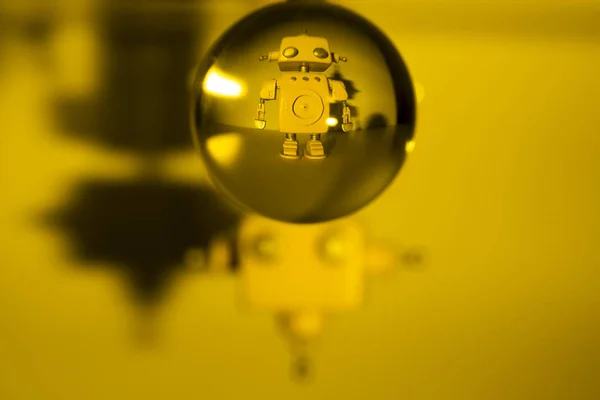 Robot na żółtym tle i za szklaną piłką. — Zdjęcie stockowe