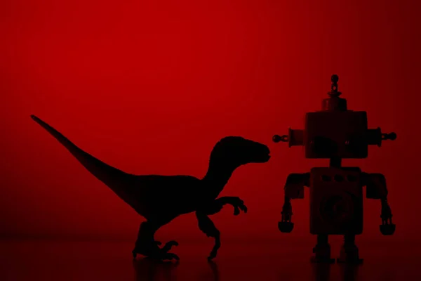 Silhuett av en Dinosaur med en robot på en rødfarget bakgrupp. – stockfoto