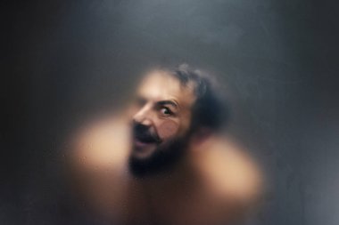 Buzlu cam arkasında bir gözü ile ürpertici görünümlü adam.