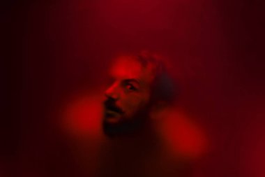 Buzlu cam arkasında bir gözü ile ürpertici görünümlü adam.