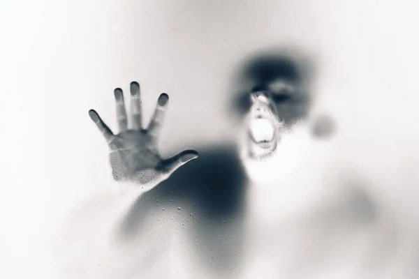 Creepy looking man is screaming behind a frosted glass. — Stock Photo, Image