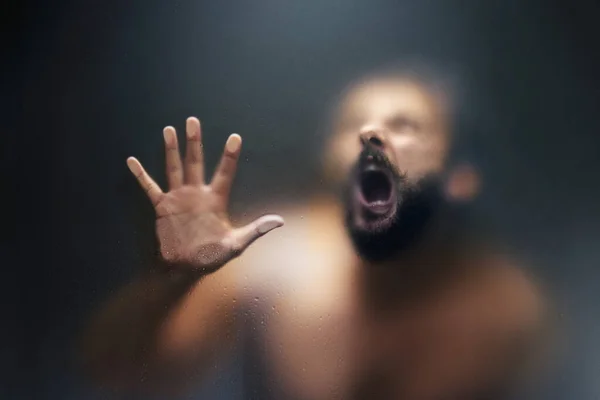 Hombre de aspecto espeluznante está gritando detrás de un vidrio helado . — Foto de Stock