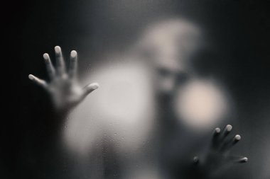 Ürkütücü adam buzlu camın arkasına bakıyor ve elinde tutuyor. 