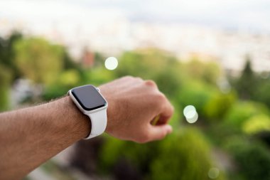 İzmir, Türkiye - 11 Haziran 2020: Apple markasının 5 'inci nesil beyaz renkli Apple saatini bir erkeğin bileğinde ve yeşil arka planda yakın çekim.