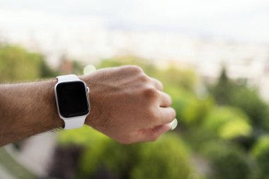 İzmir, Türkiye - 11 Haziran 2020: Apple markasının 5 'inci nesil beyaz renkli Apple saatini bir erkeğin bileğinde ve yeşil arka planda yakın çekim.