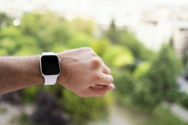 İzmir, Türkiye - 11 Haziran 2020: Apple markasının 5 'inci nesil beyaz renkli Apple saatini bir erkeğin bileğinde ve yeşil arka planda yakın çekim.