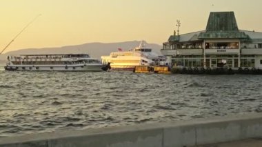 İzmir, Türkiye - 4 Temmuz 2020: İzmir 'de gün batımında İzmir' de balıkçılık yapan bir balıkçı ile Konak Ferry İstasyonu 'nun görüntüleri.