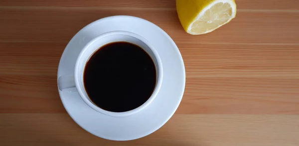 A Cup of coffee and half a lemon on the wooden table. Suitable for background and mockups
