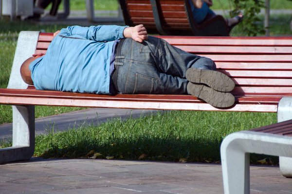 homeless man sleeping on park bench in sunny day
