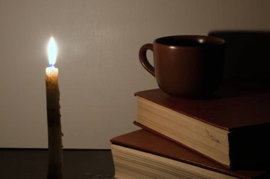 Mum ışığı seramik bardağa düşer ve bulanık arka plana eski kitaplar düşer.