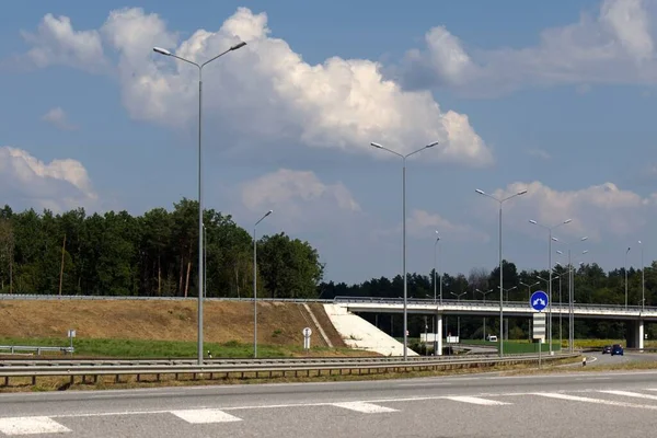 Otobanda üstgeçit, yol boyunca aydınlatma sütunları, bulanık ön plan, beyaz bulutlu mavi gökyüzü.