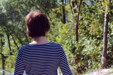 Yeşil ormanın bulanık arka planında çizgili tişörtlü bir kız. Arkadan görünüm