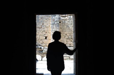 Bir kızın silueti, açık bir kapı aralığında, bulanık bir arka planda, güneş ışığıyla dolu bir verandaya karşı.