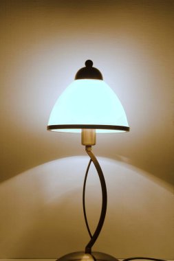 Gece lambası yumuşak sıcak ışıkla parlar ve duvardaki gölgeleri yansıtır.