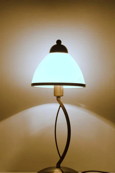 Home bedside table night lamp shines with soft warm light and reflects shadows on the wall