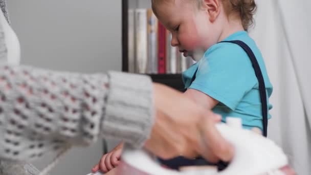 Vestiti da donna stirati. Giovane donna è abbigliamento da stiro, bambino piccolo ragazzo è seduto accanto a asse da stiro — Video Stock