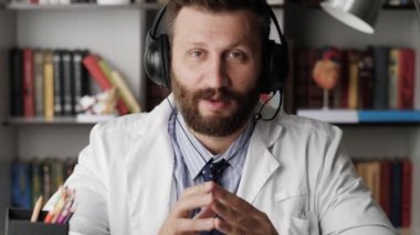 Optometrist kamerayla konuşuyor. Beyaz önlüklü çekici sakallı göz doktoru kameraya bakarken bir şeyi açıklıyor, gözler için jimnastik yapıyor.