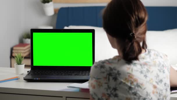 Γυναίκα κάθεται στο γραφείο στην κρεβατοκάμαρα, κοιτάζει φορητό υπολογιστή πράσινη οθόνη και μιλάει σε κάποιον μέσω διαδικτυακών βίντεο επικοινωνιών, μερικές φορές κρατώντας σημειώσεις στο σημειωματάριο. Κοντινό πλάνο — Αρχείο Βίντεο