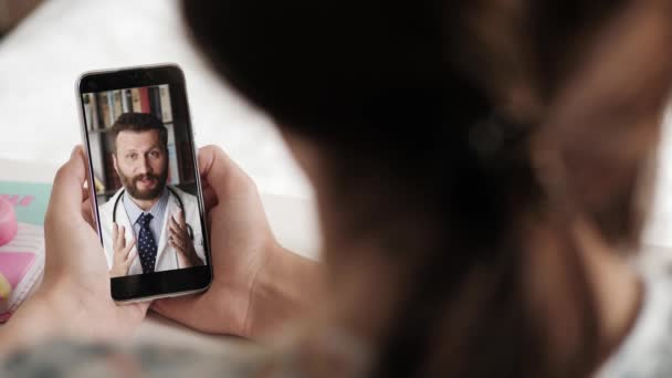 Kvinna håller telefonen i sina händer och talar på video online-anslutning med mannen i vit rock till läkare. Onlinekonsultation, distanshjälp, psykoterapi. Närbild — Stockvideo
