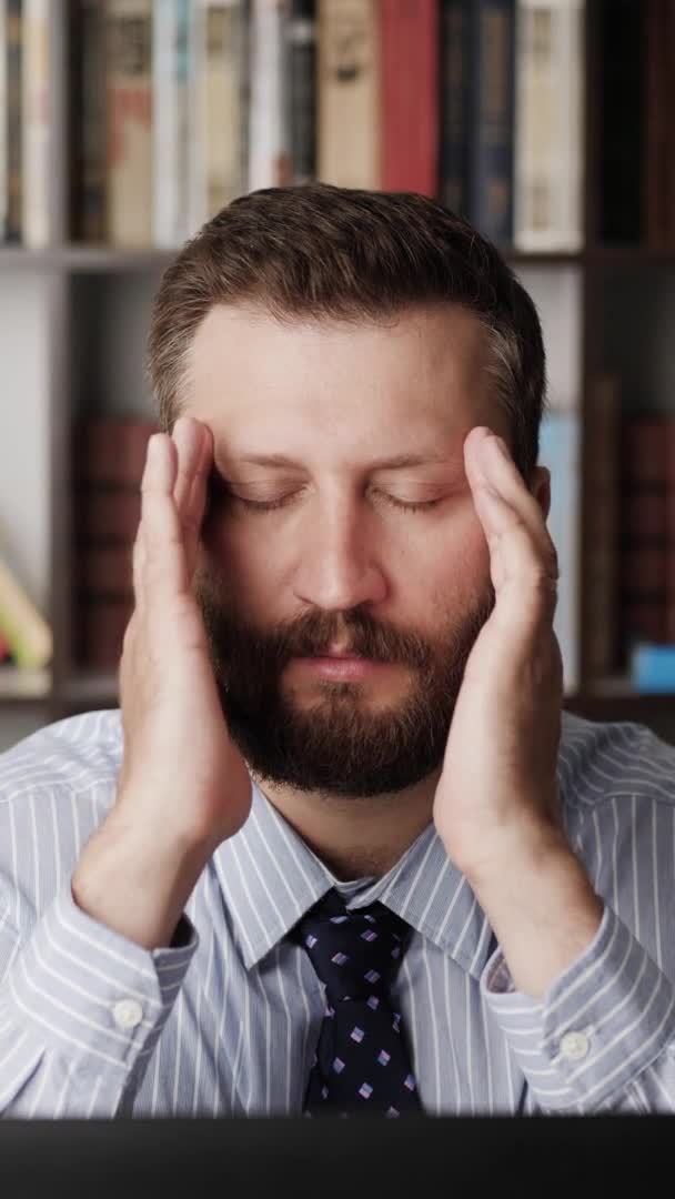 Dolor de cabeza. Orientación vertical del hombre barbudo molesto en el lugar de trabajo que experimenta dolores de cabeza, toca la parte temporal y el área de los ojos con las manos. Estrés, fatiga, hipertensión, concepto de migraña — Vídeo de stock