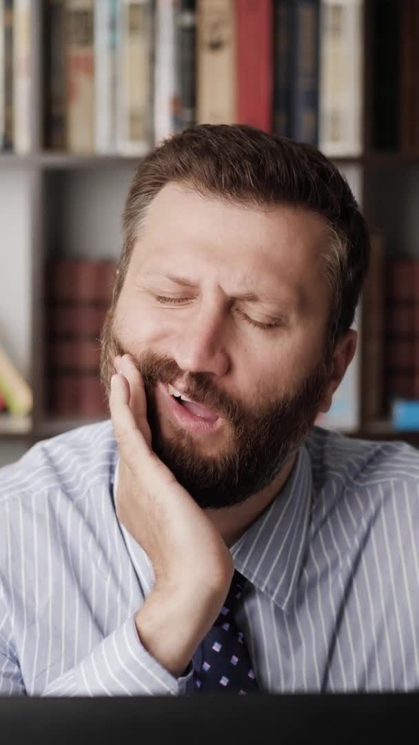 J'ai mal aux dents. Orientation verticale de l'homme barbu sur le lieu de travail, il éprouve de fortes douleurs dans les dents et touche son visage avec la main. Caries, pulpiite, concept de maladie des gencives — Video