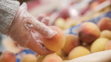 Eldivenli kadın süpermarkette sepetten meyve şeftalisi topluyor. Yakın plan.