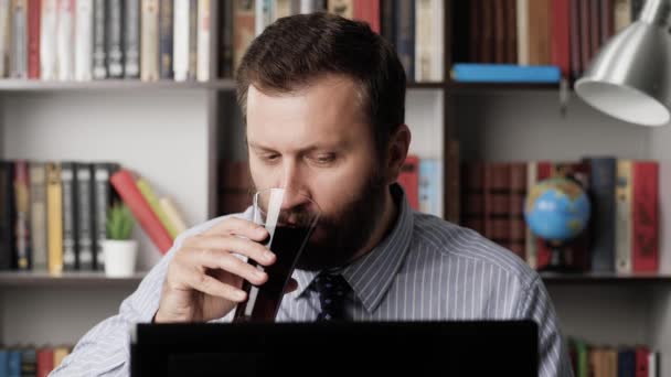 Μεσημεριανό διάλειμμα, σνακ στη δουλειά, φαστ φουντ. Ο άνθρωπος στο χώρο εργασίας κοιτάζει την οθόνη του φορητού υπολογιστή, πληκτρολογεί στο πληκτρολόγιο και τρώει σάντουιτς με γλυκό ανθρακούχο ποτό. Κοντινό πλάνο — Αρχείο Βίντεο